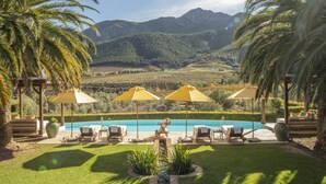 Un espace aménagé au bord de la piscine, avec des chaises longues et des parasols, une terrasse en bois et une vue sur les montagnes.