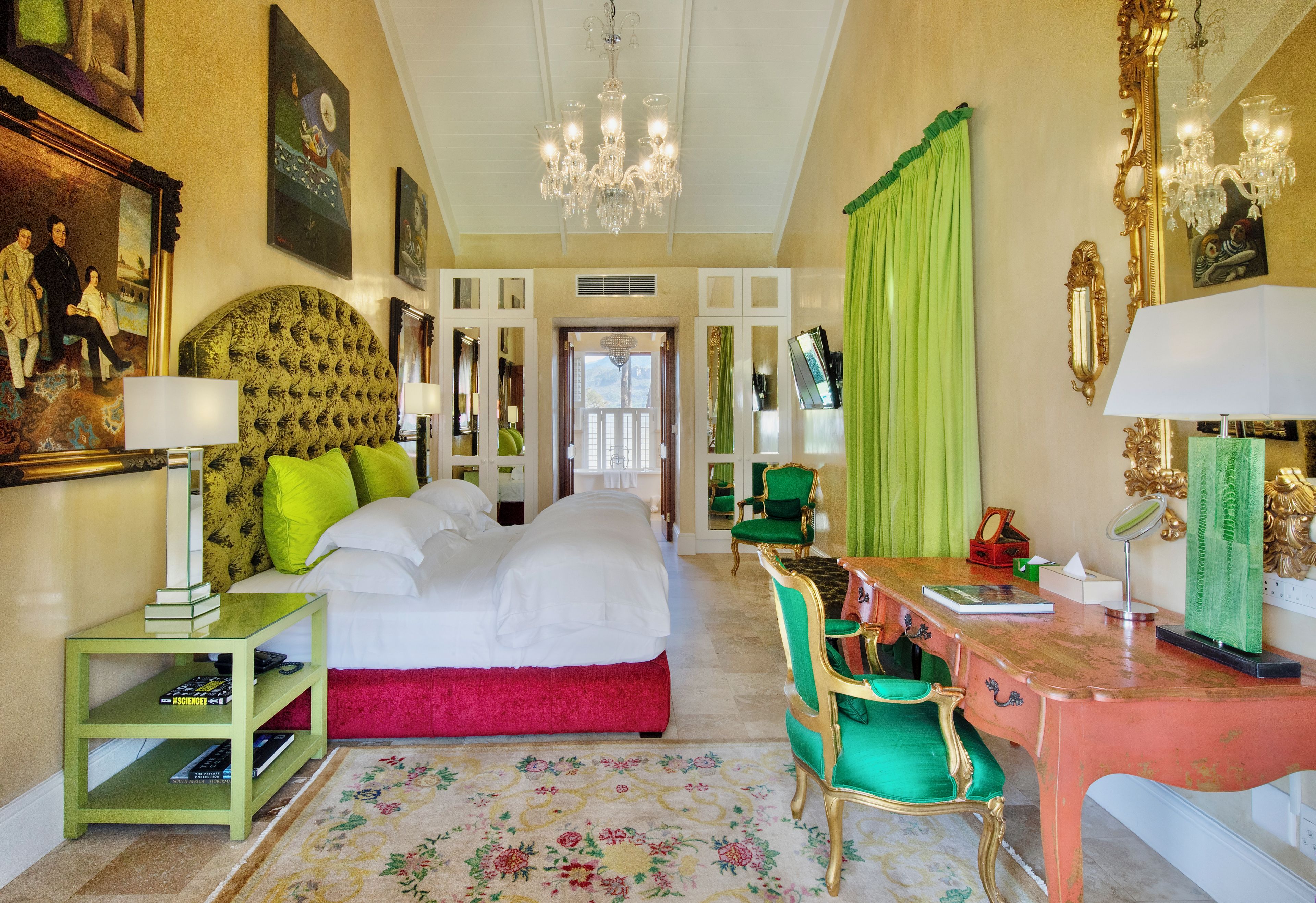 Une chambre d’hôtel avec un grand lit, un bureau avec une chaise, un miroir et un lustre.