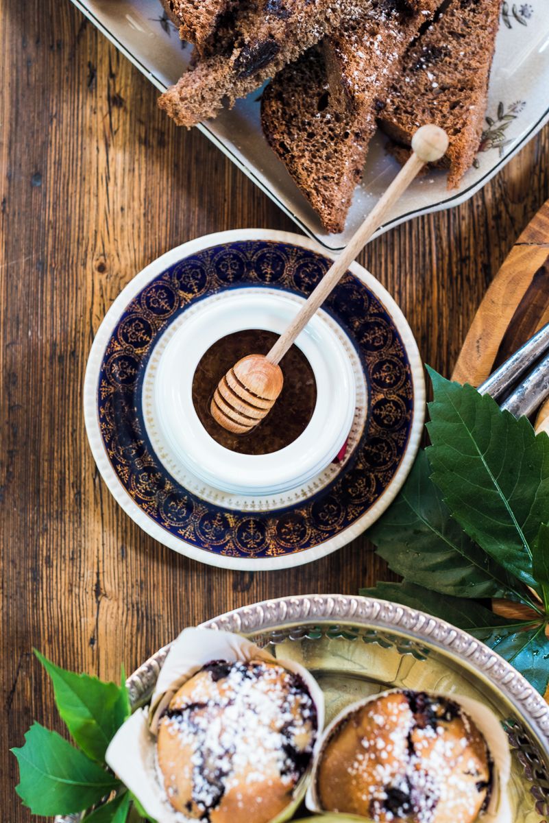 A wooden table with a decorative plate containing a honey dipper and a jar of honey, alongside a plate with pastries.