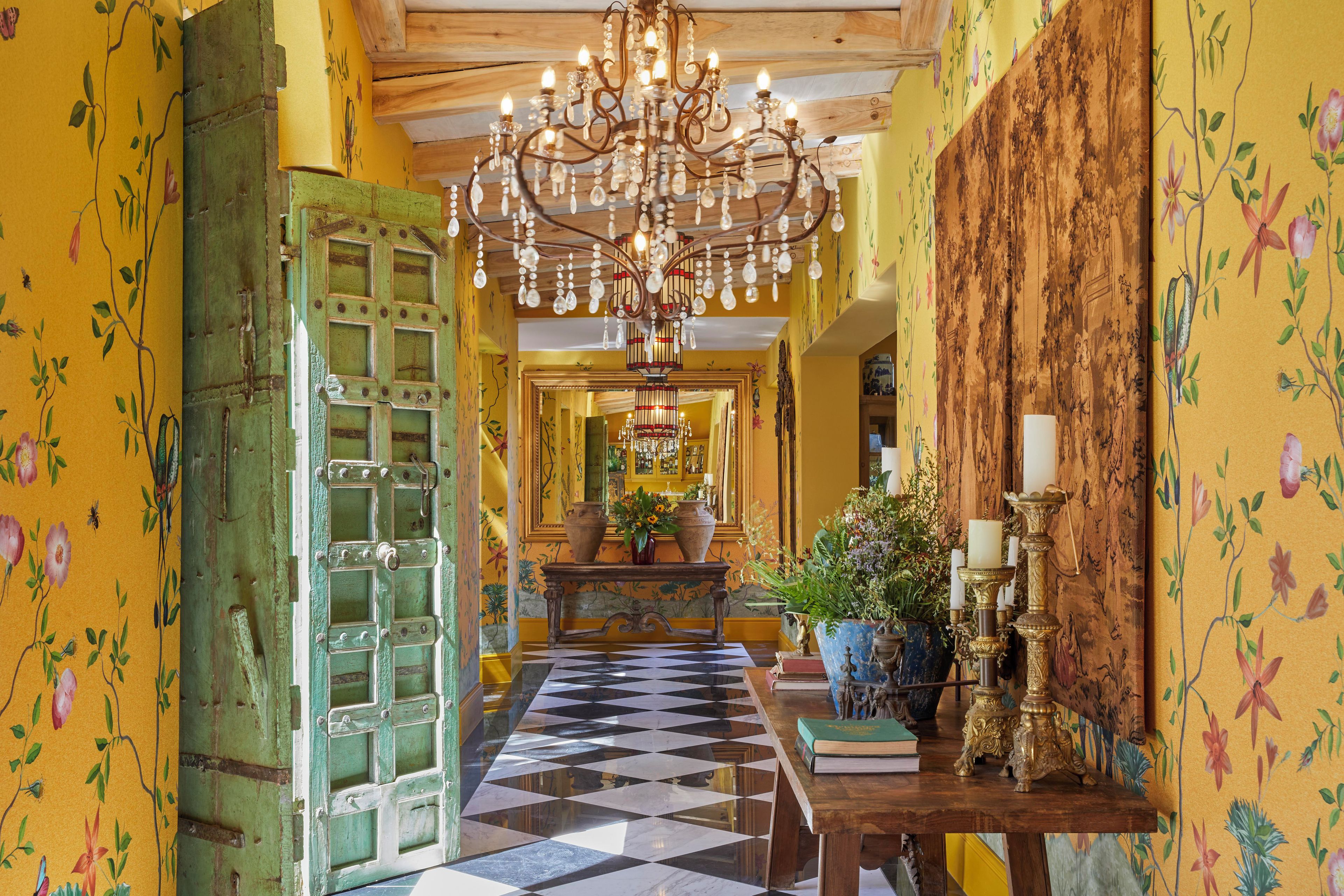 A hallway with a checkered floor, a chandelier, and floral wallpaper.