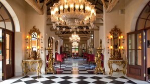 Un vaste hall d’entrée avec un sol à carreaux noirs et blancs, de somptueux lustres et des miroirs encadrés d’or.