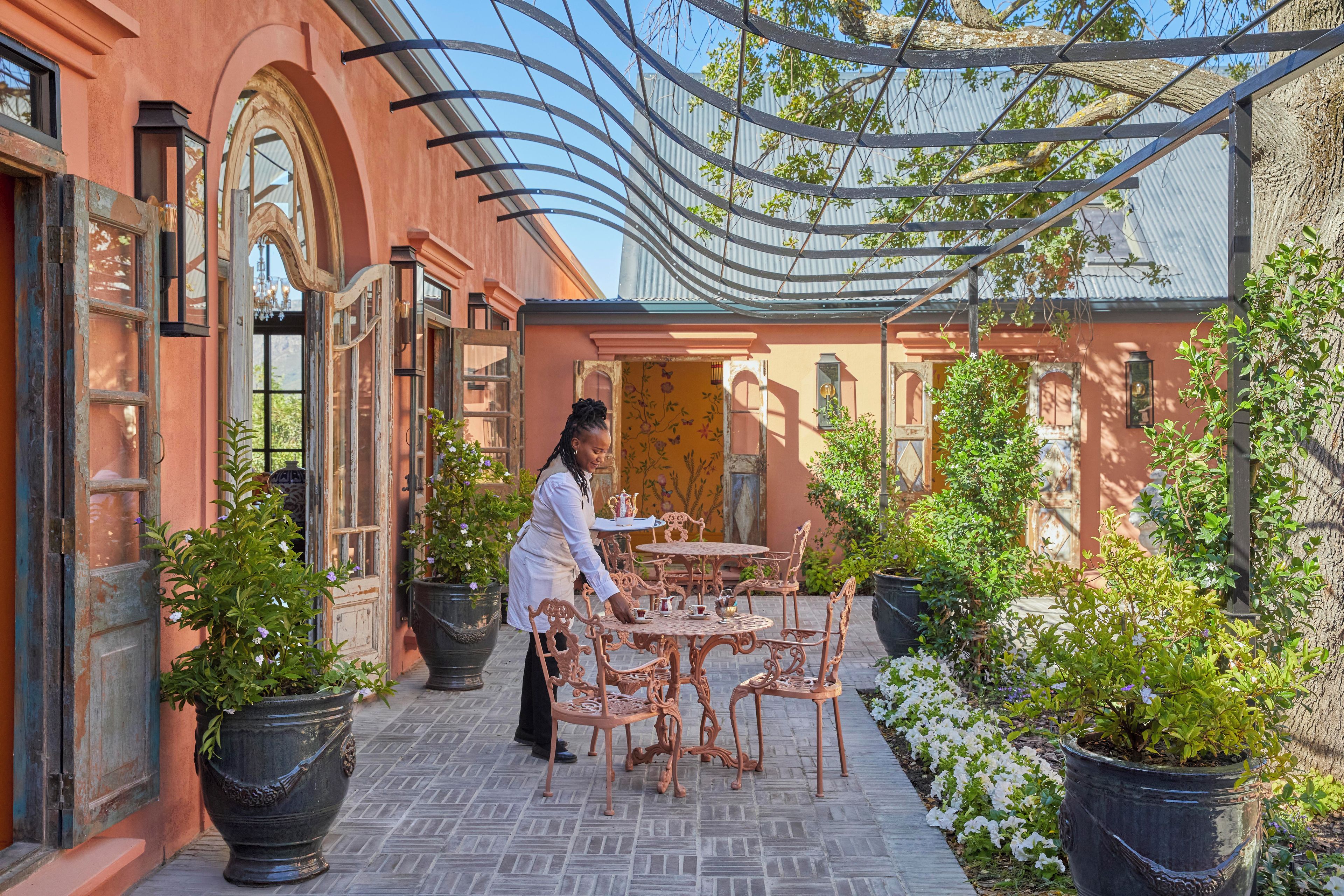 A courtyard with a covered seating area, potted plants, and a building with arched windows.