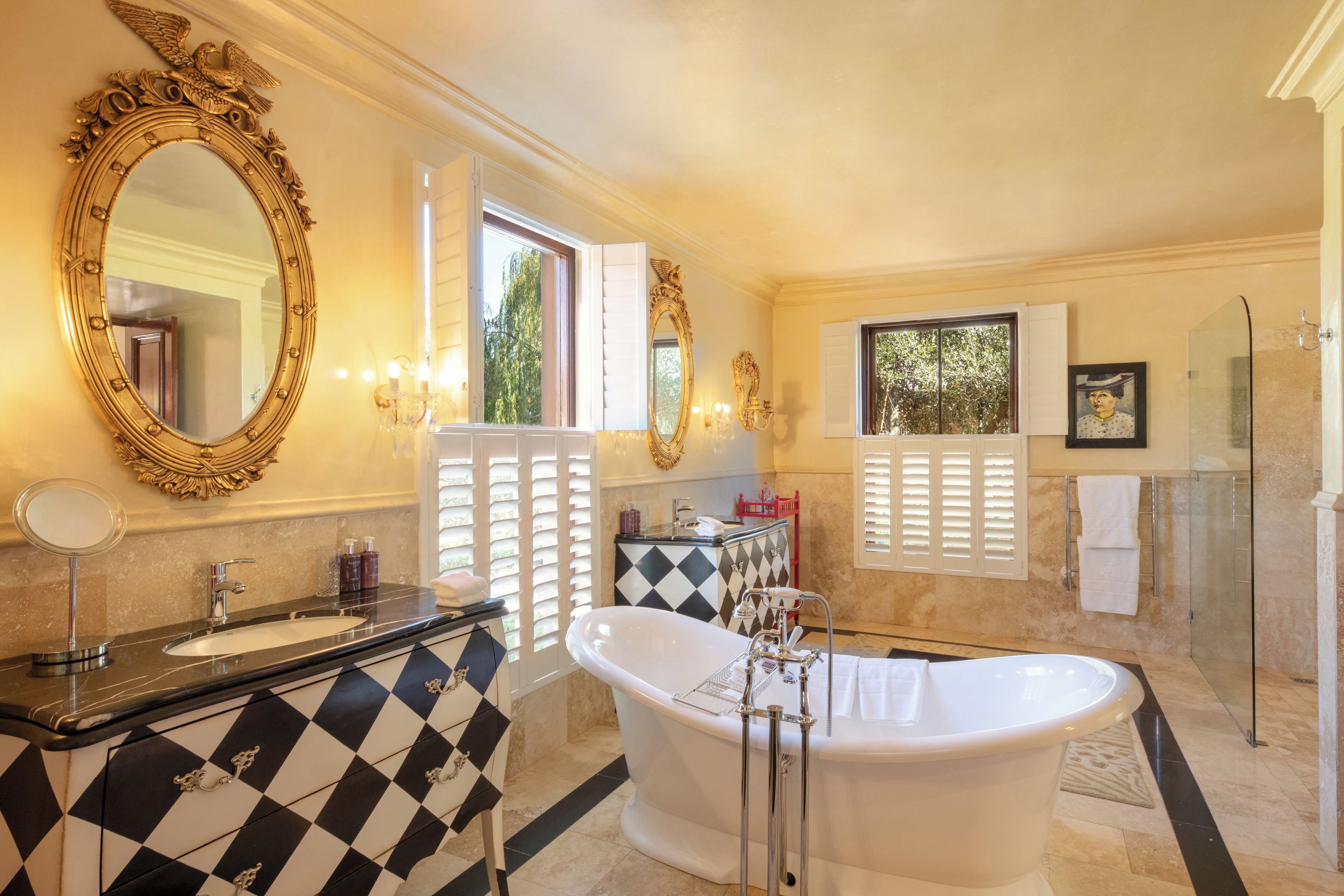 A luxurious bathroom with a freestanding bathtub, a large ornate mirror, and a vanity with a checkered tile backsplash.