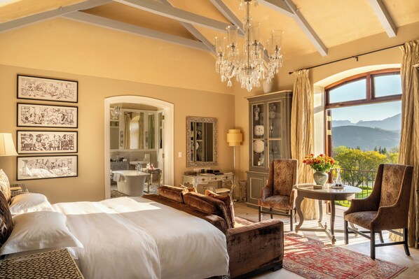 Une chambre spacieuse avec un grand lit, un coin salon, un lustre et une vue sur l’extérieur.