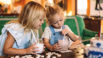 Two children sitting at a table with drinks and dominoes.