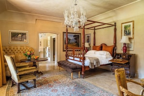 Un dormitorio tradicional con cama con dosel, una zona de estar con una silla y una mesa, y un candelabro.