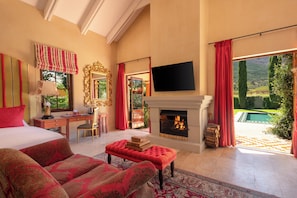 Un dormitorio amplio con una cama grande, una zona de estar con un reposapiés rojo, chimenea y televisión.