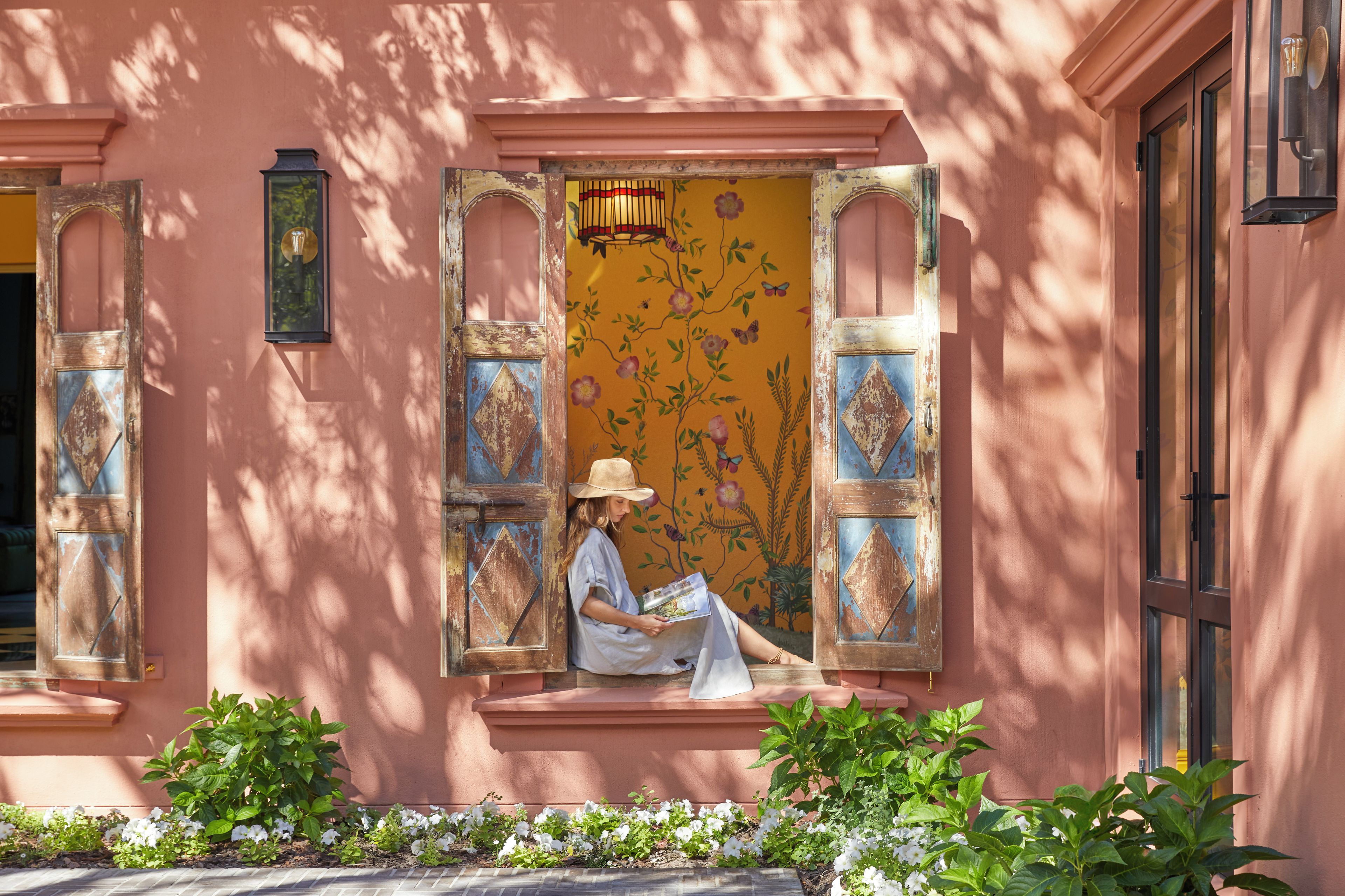 A person sitting on a bench outside a building with a floral mural on the wall.