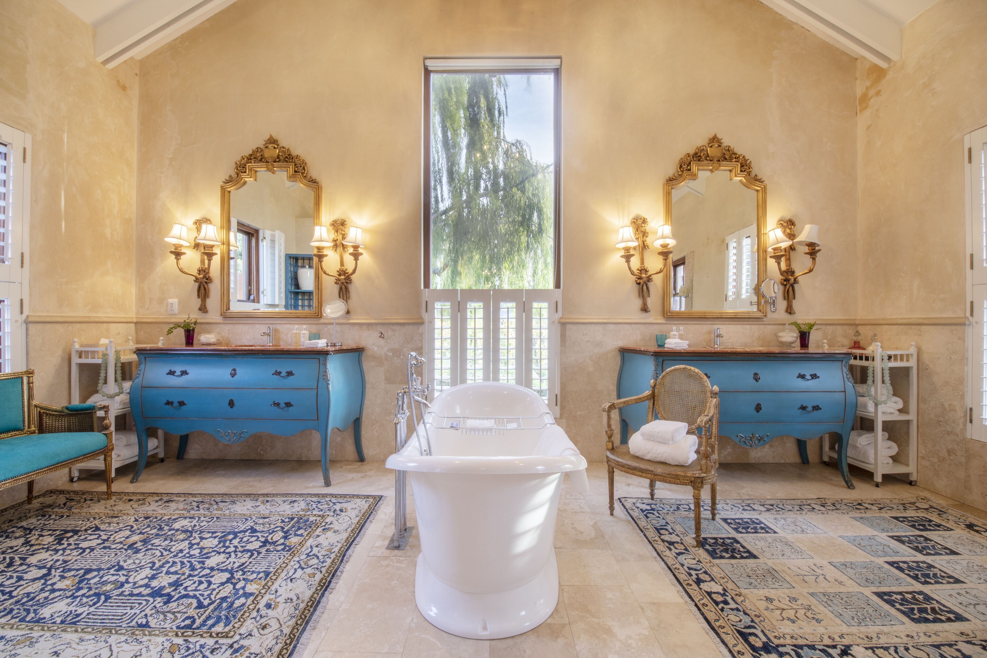 A bathroom with a freestanding bathtub, two sinks with blue cabinets, and ornate mirrors.