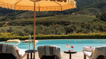 Zona junto a la piscina con sillones de descanso y una sombrilla, con vistas a un paisaje de viñedos.
