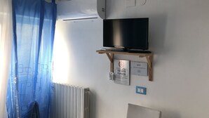 Una habitación con televisión sobre un soporte de madera, un radiador, una cortina azul y aire acondicionado instalado en la pared.