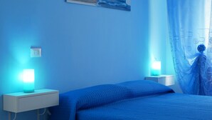 Una habitación con cama, lámparas de noche, un enchufe y un cuadro en la pared.