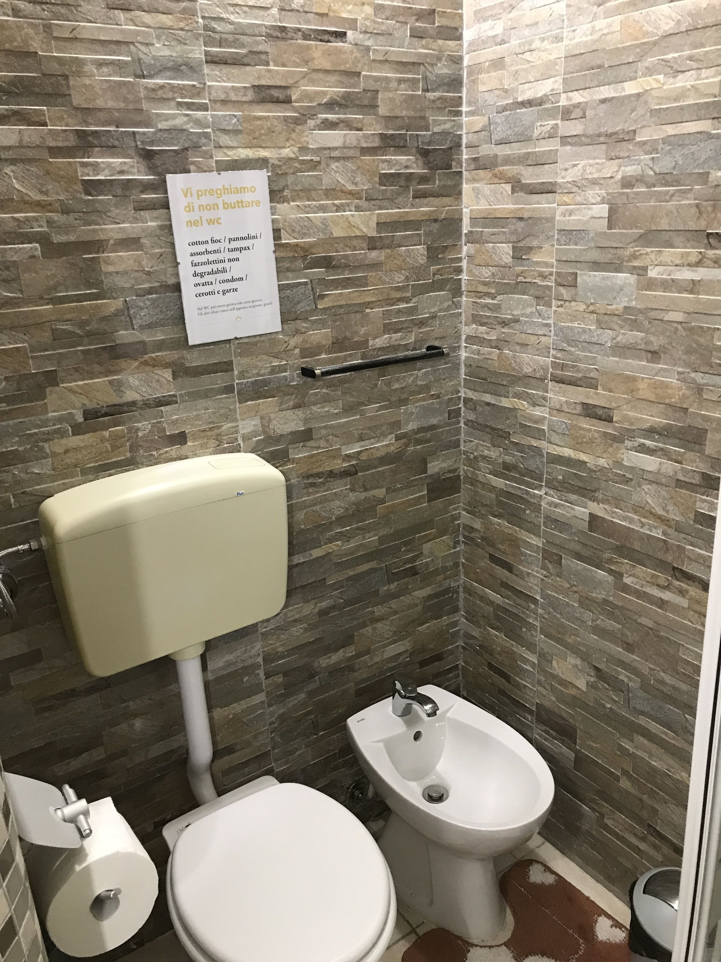 Un baño con inodoro, bidé y pared de piedra.