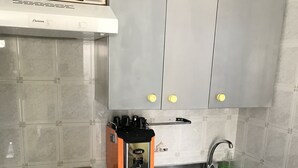 Una cocina con estufa a gas, máquina de café espresso, pileta y armarios grises con detalles en amarillo.
