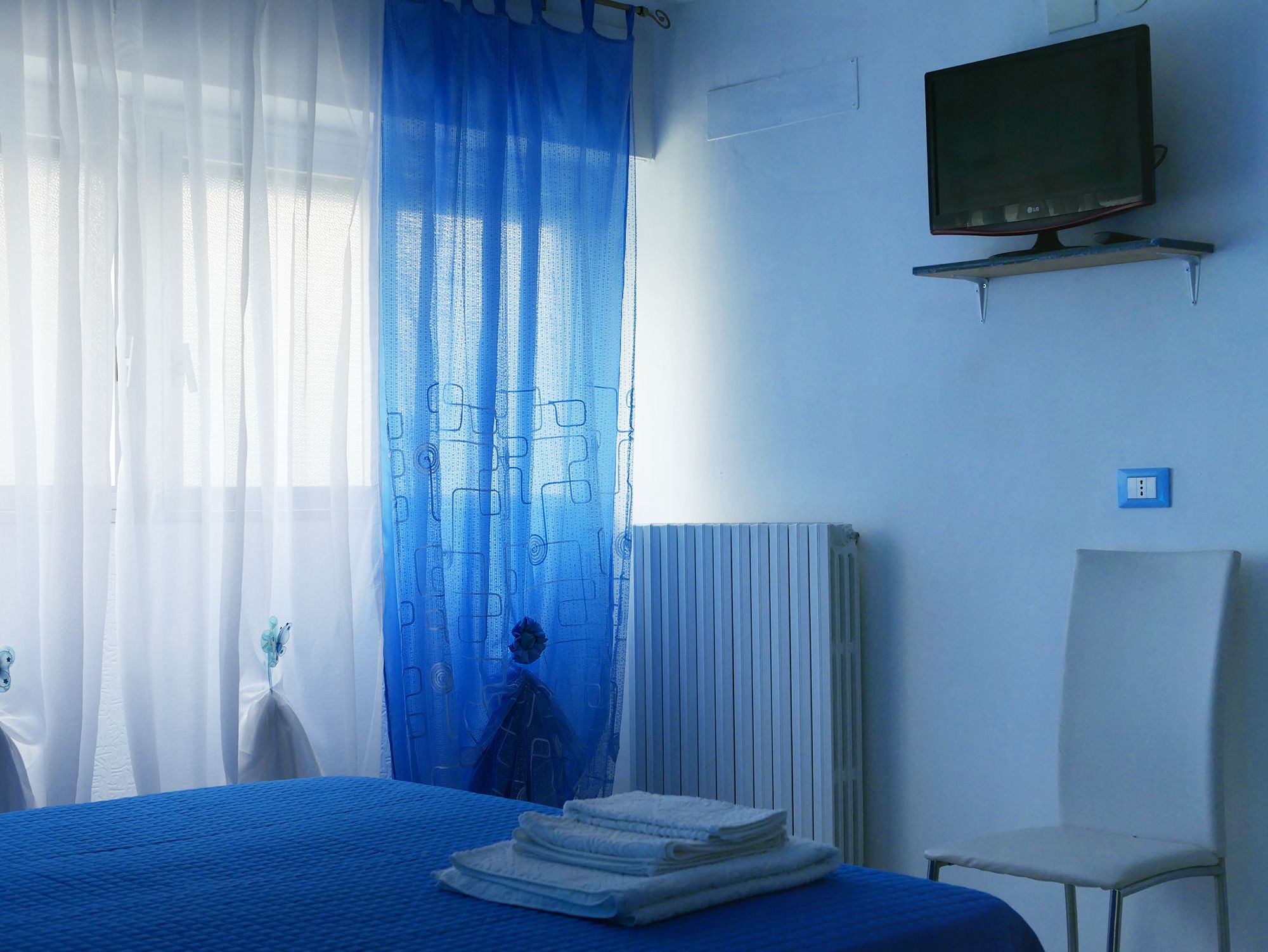 A hotel room with a bed, a chair, a television on a stand, and a radiator.