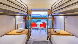 A train compartment with two beds, a table with red chairs, and a view of a landscape through a window. - HI Ponte de Lima - Pousada de Juventude - Hostel (Ponte de Lima)