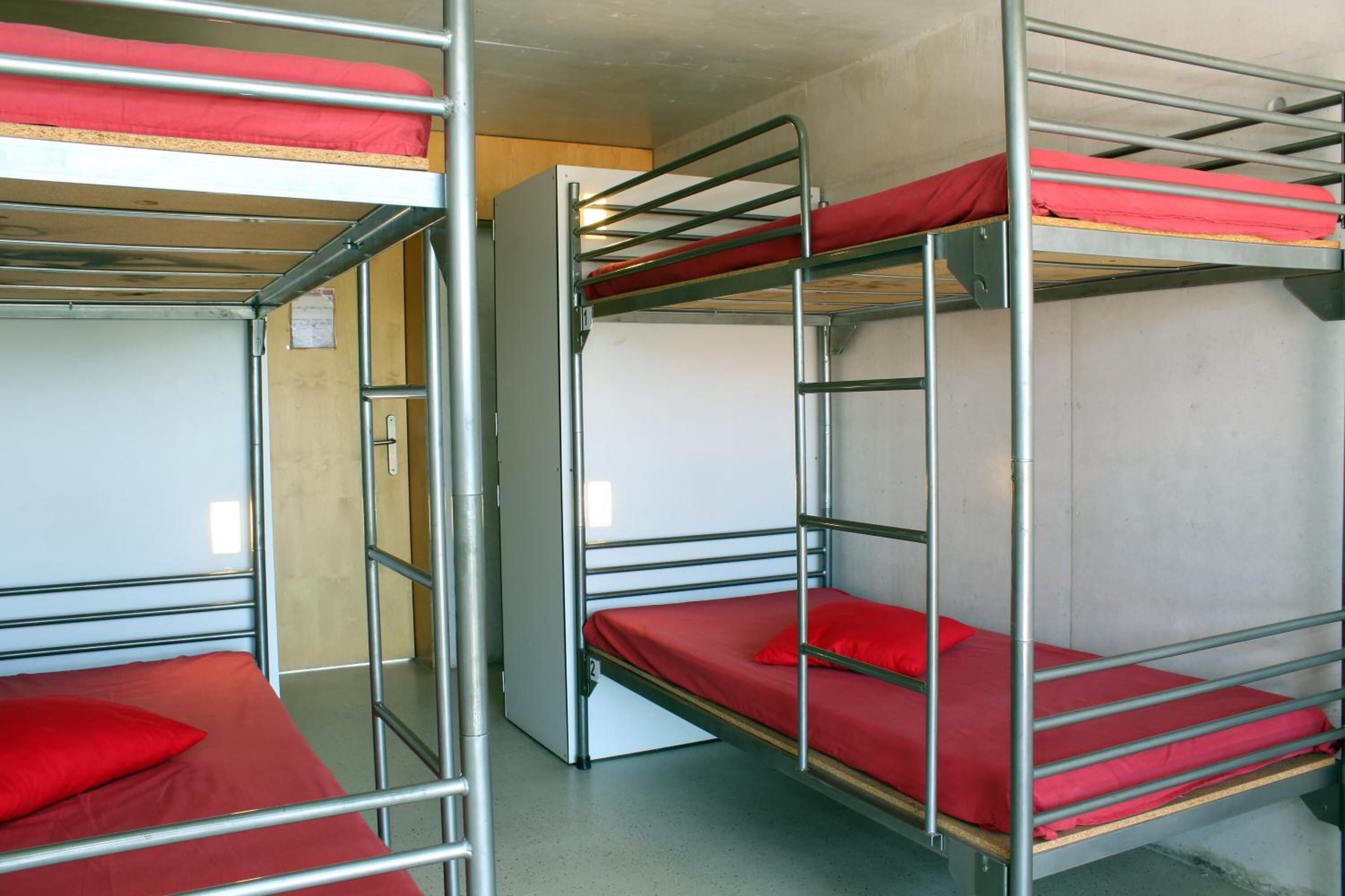 Un dormitorio con literas, cada una con colchón y almohada rojos.