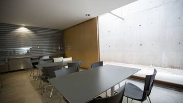 Un salón de conferencias con una larga mesa y sillas, una kitchenette y un ventanal con vistas.