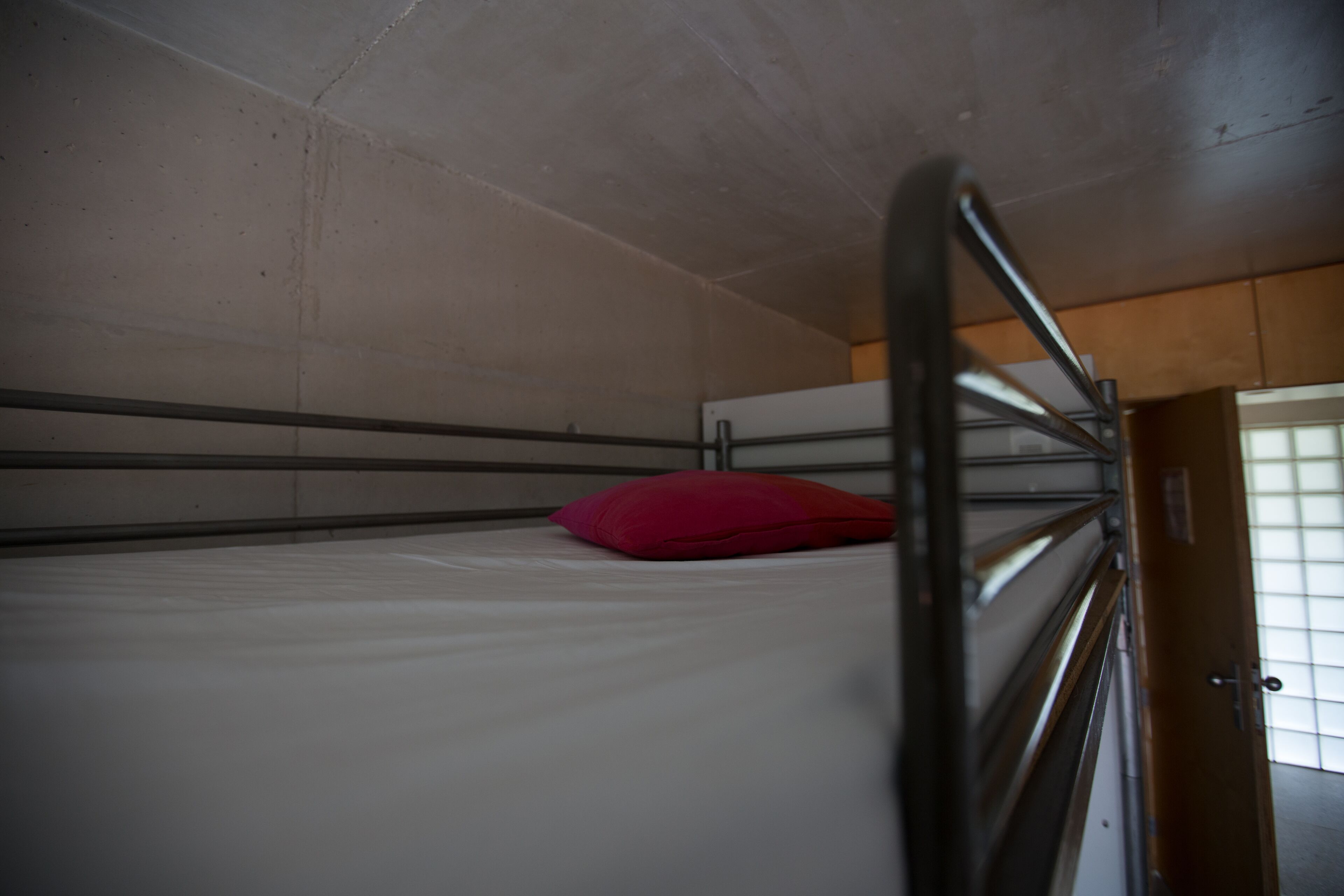 Una cama litera con almohada roja, barandillas de metal y una puerta de madera.
