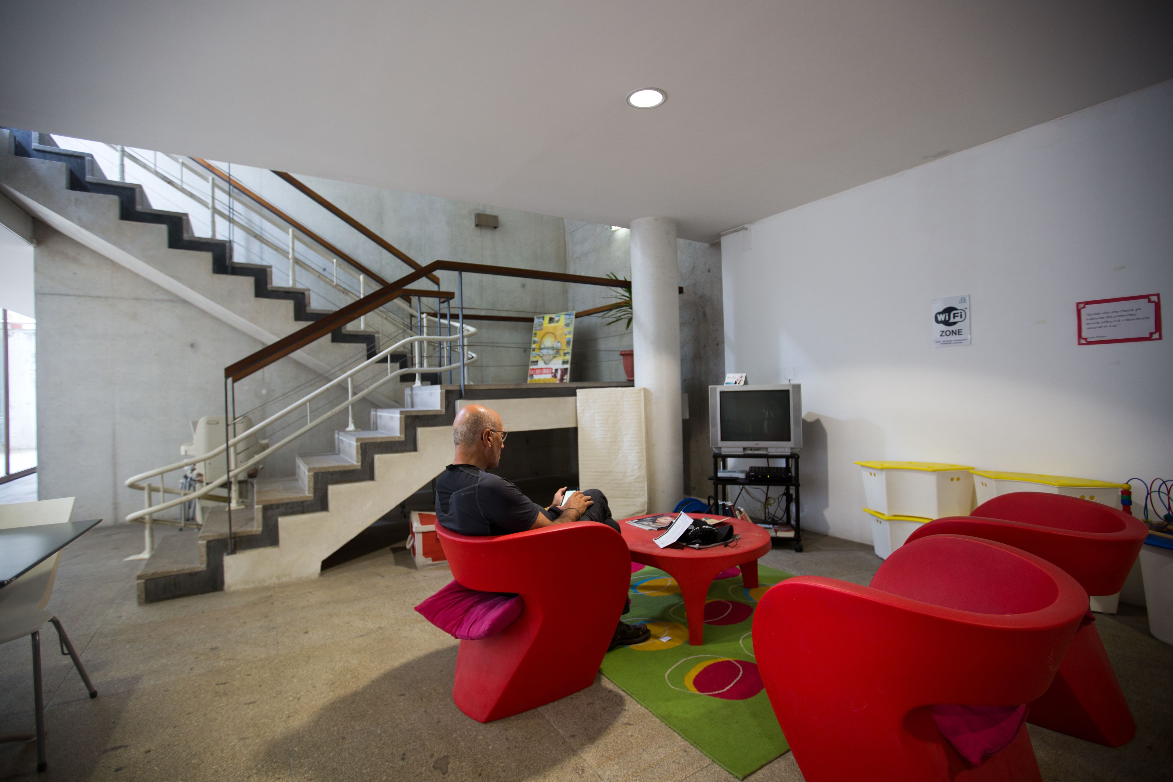A modern interior with a staircase, red chairs, a table, and a television.