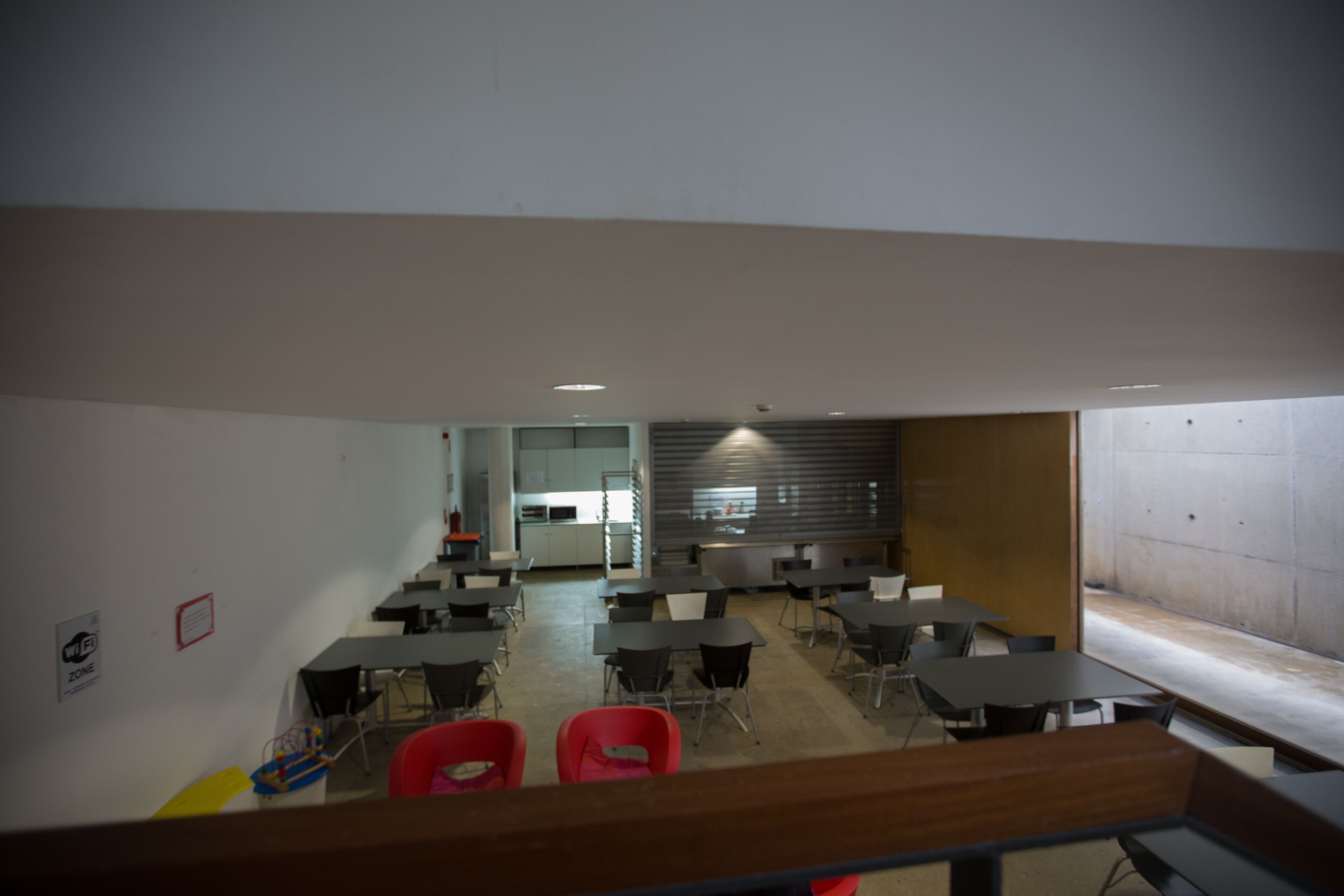 Un espace de restauration moderne avec des tables et des chaises, une cuisine en arrière-plan et une vue par une fenêtre.