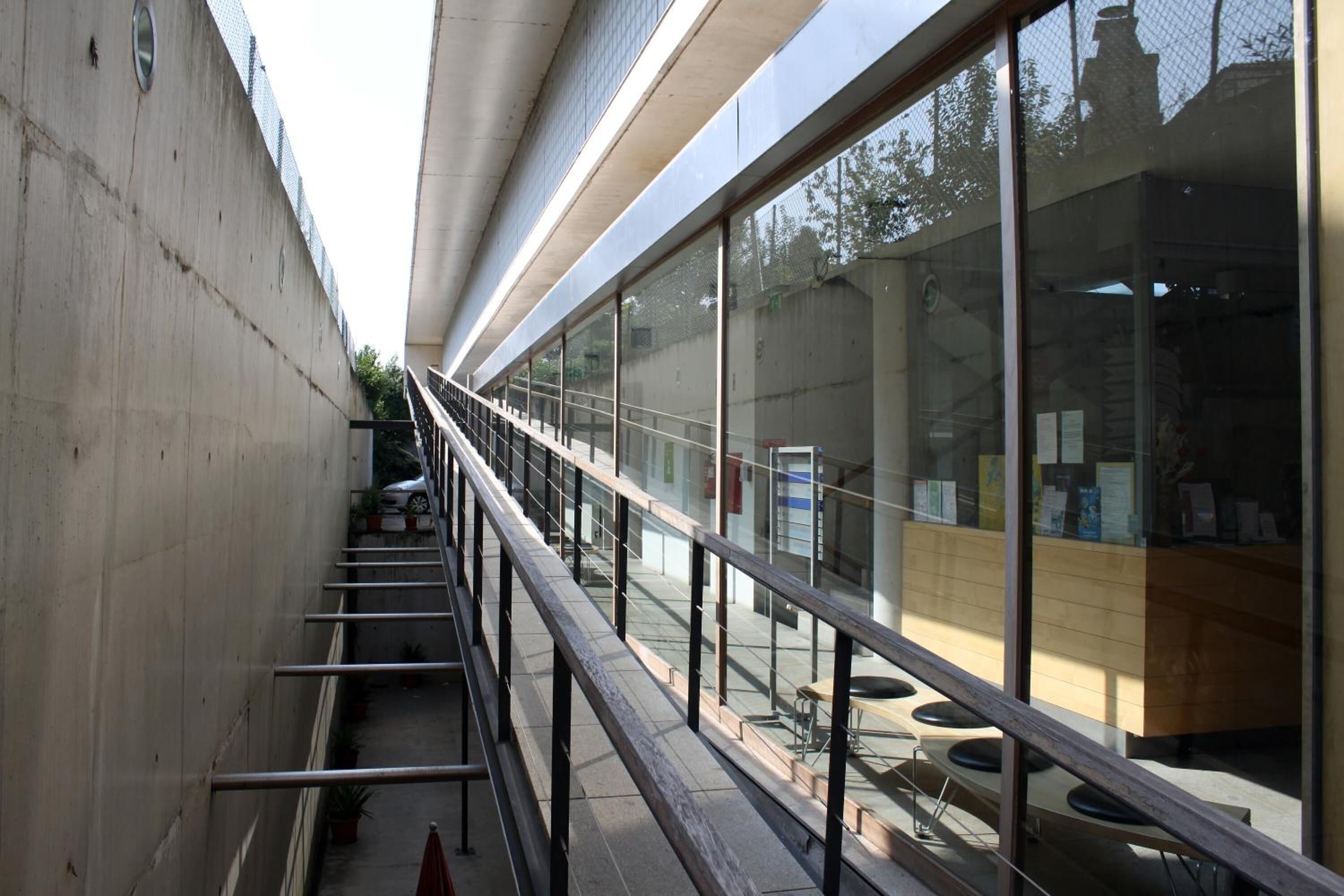 A modern building with a glass facade, outdoor seating area, and a staircase leading to an upper level.