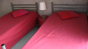 Quarto com duas camas de solteiro, cada uma com colcha e almofadas vermelhas. Uma mesa de cabeceira individual com abajur fica entre as camas.