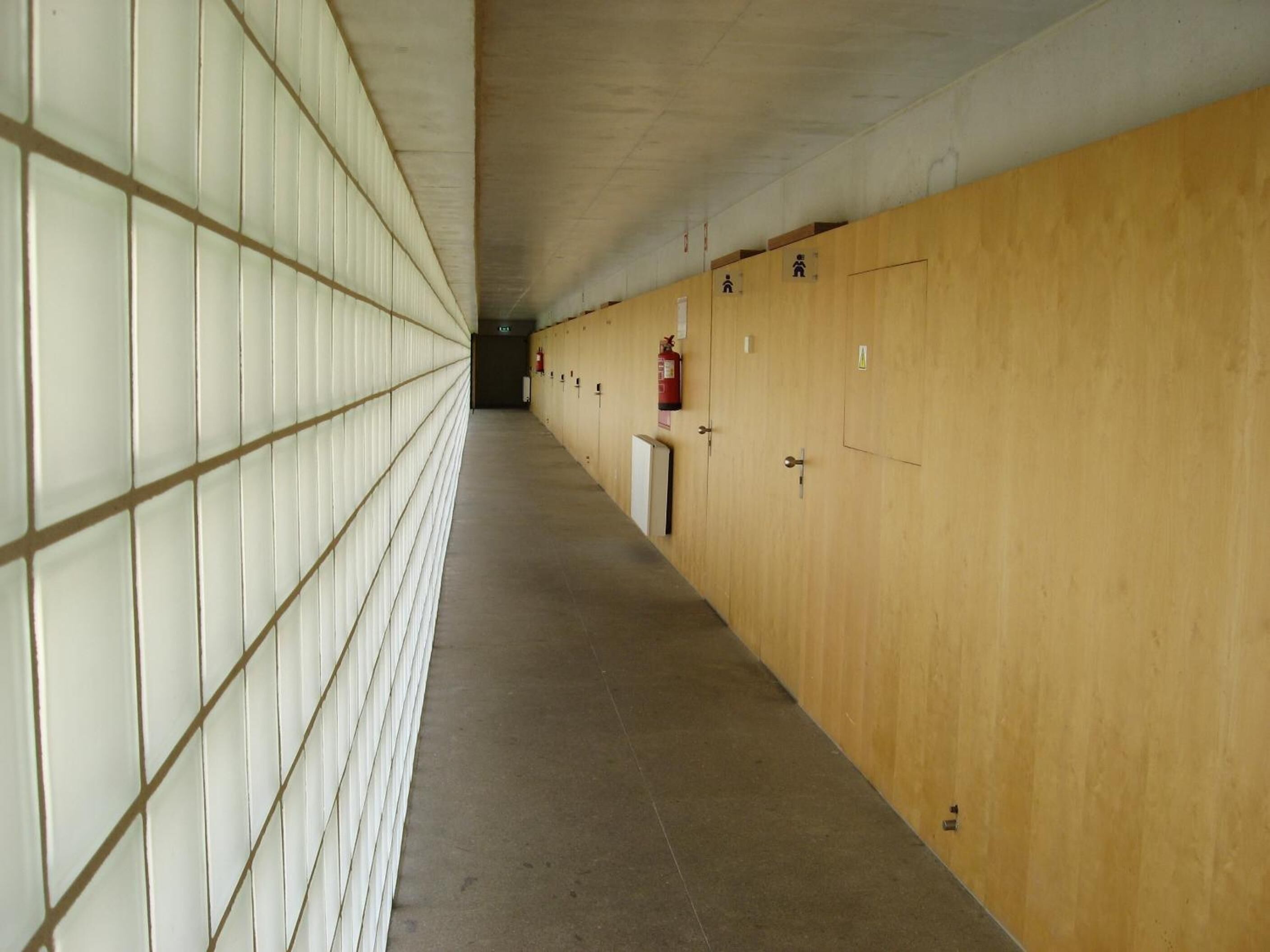 A long corridor with lockers on one side and a fire extinguisher mounted on the wall.