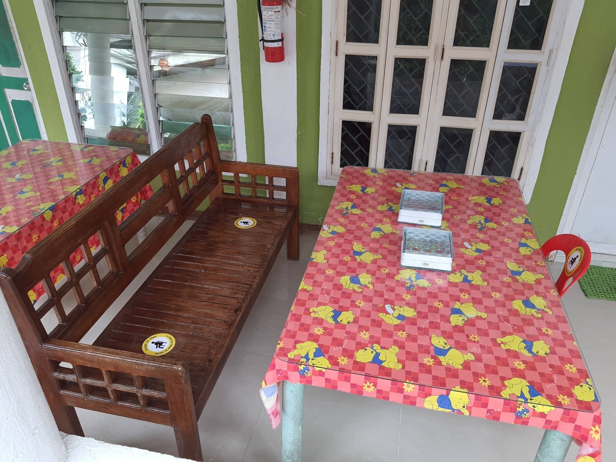 A room with a wooden bench and two tables, both covered with red checkered tablecloths featuring cartoon characters.