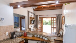 Una cocina con encimeras de granito, microondas, cafetera y lavamanos. Hay una ventana con cortinas y vistas a la vegetación.