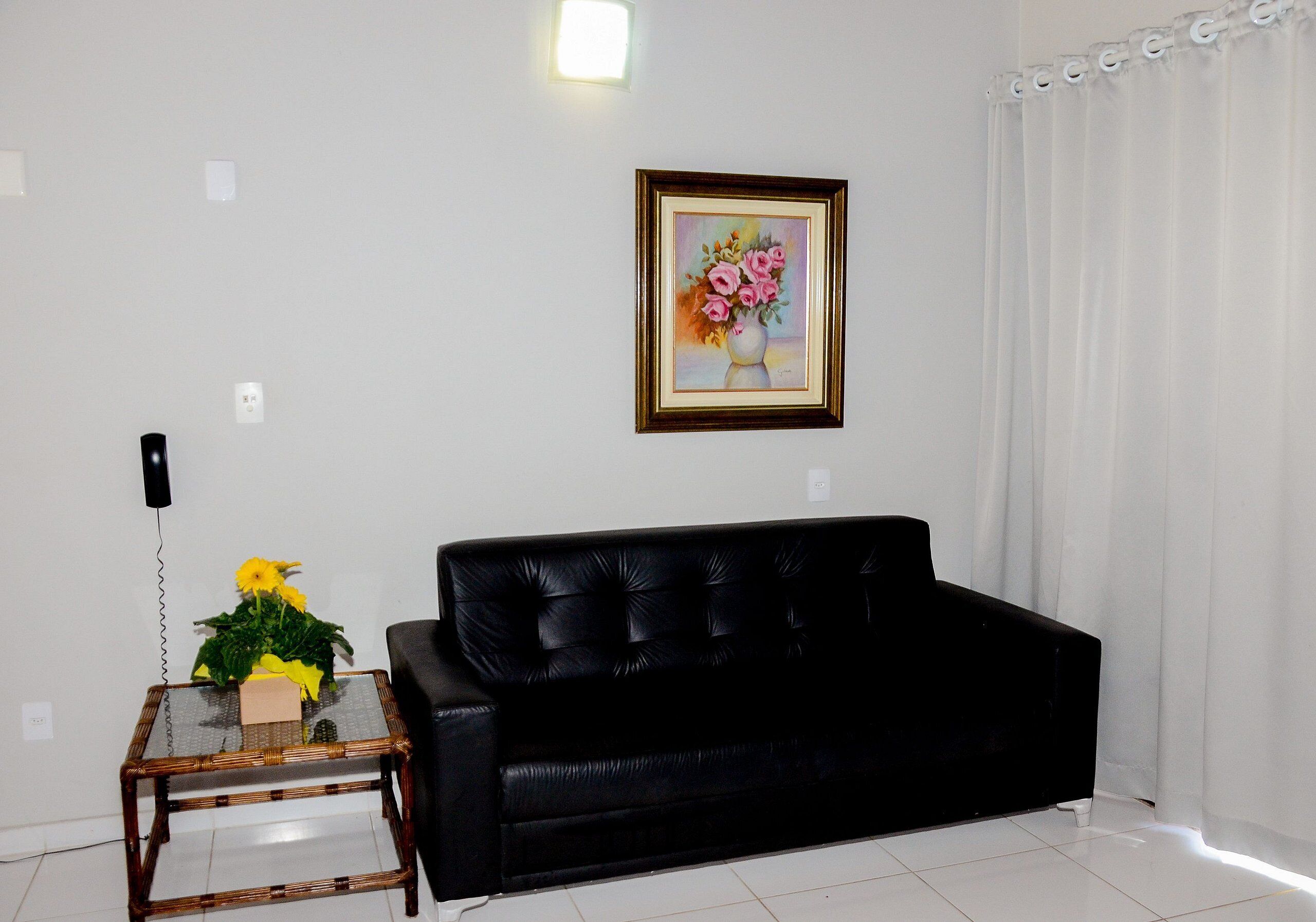 A living room with a black sofa, a glass table with a vase of flowers, and a framed painting on the wall.