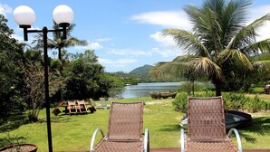 Dos sillones de mimbre mirando un lago, con una palmera y un farol al frente.