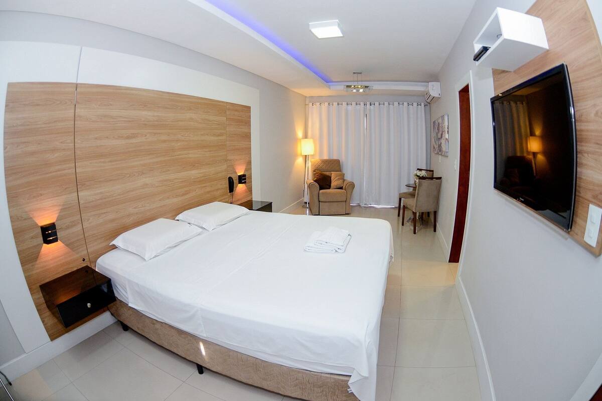 Una habitación de hotel moderna con una cama grande, mesitas de noche, un escritorio y un televisor.