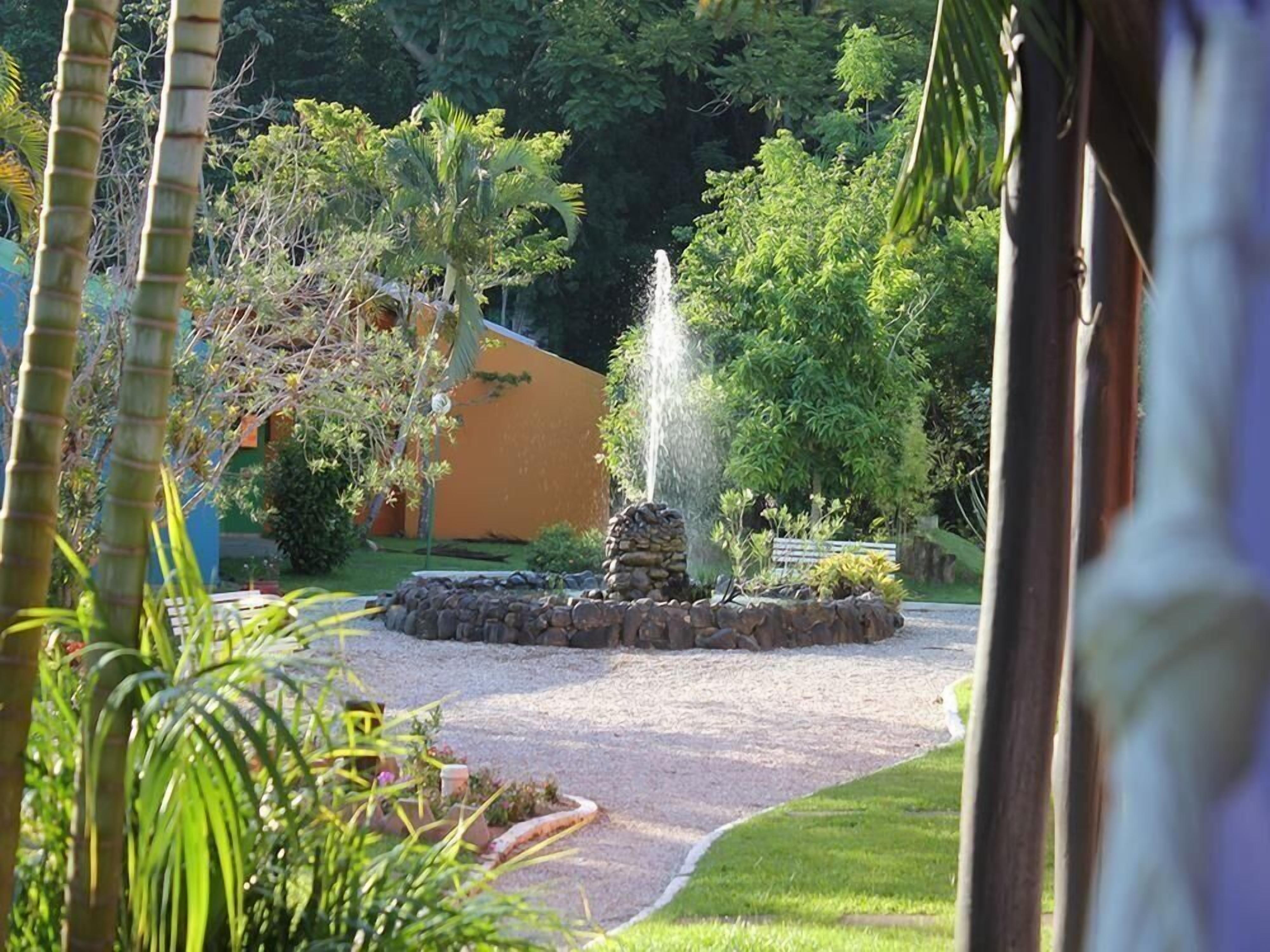 A garden with a central fountain, surrounded by a stone wall and various plants.