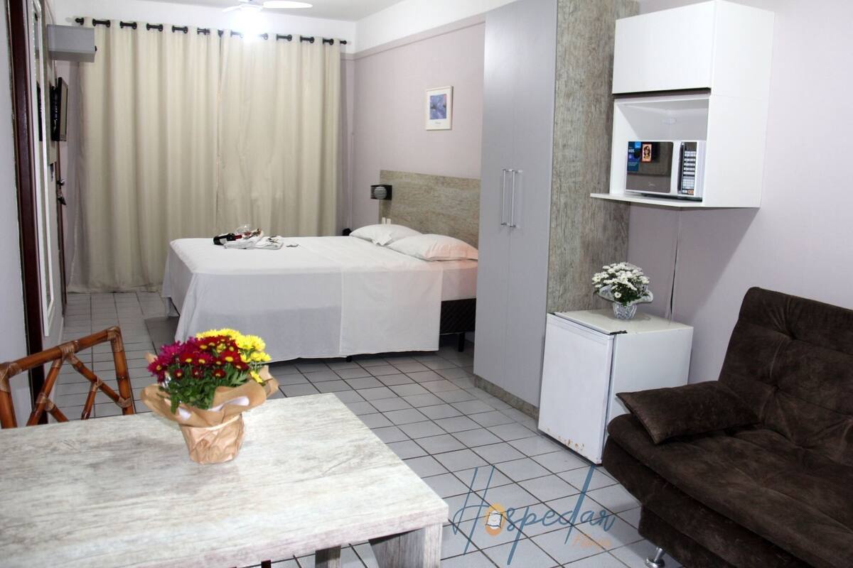 Una habitación de hotel con una cama, una pequeña mesa con un ramillete de flores, un sofá marrón, un microondas y un armario.
