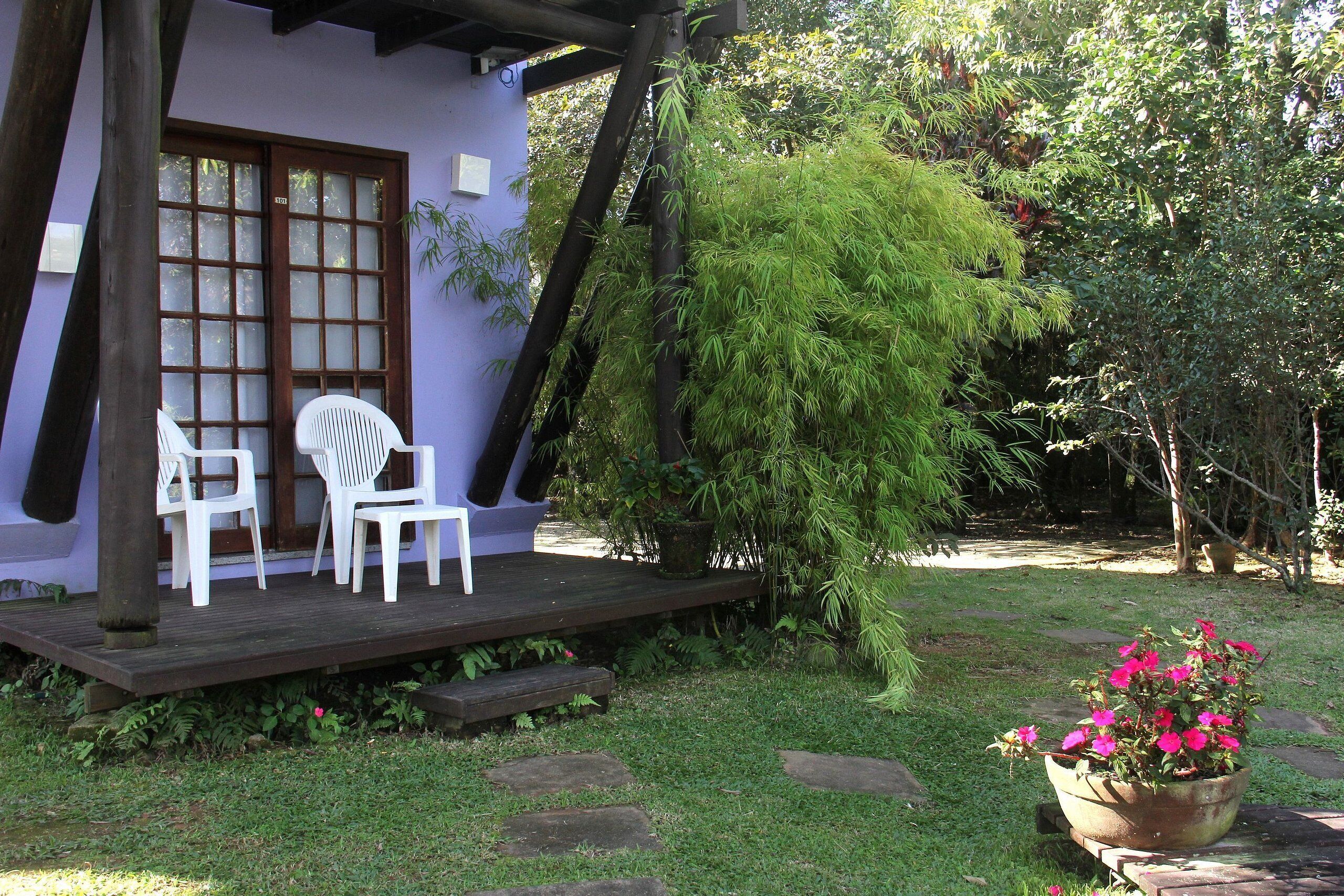 A patio with two white chairs, a wooden deck, and a potted plant with pink flowers.