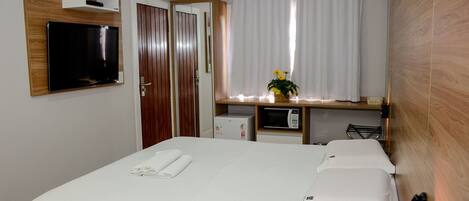 Ein Hotelzimmer mit Bett, Wandfernseher, kleinem Schreibtisch mit Mikrowelle und einem Fenster mit Vorhängen.