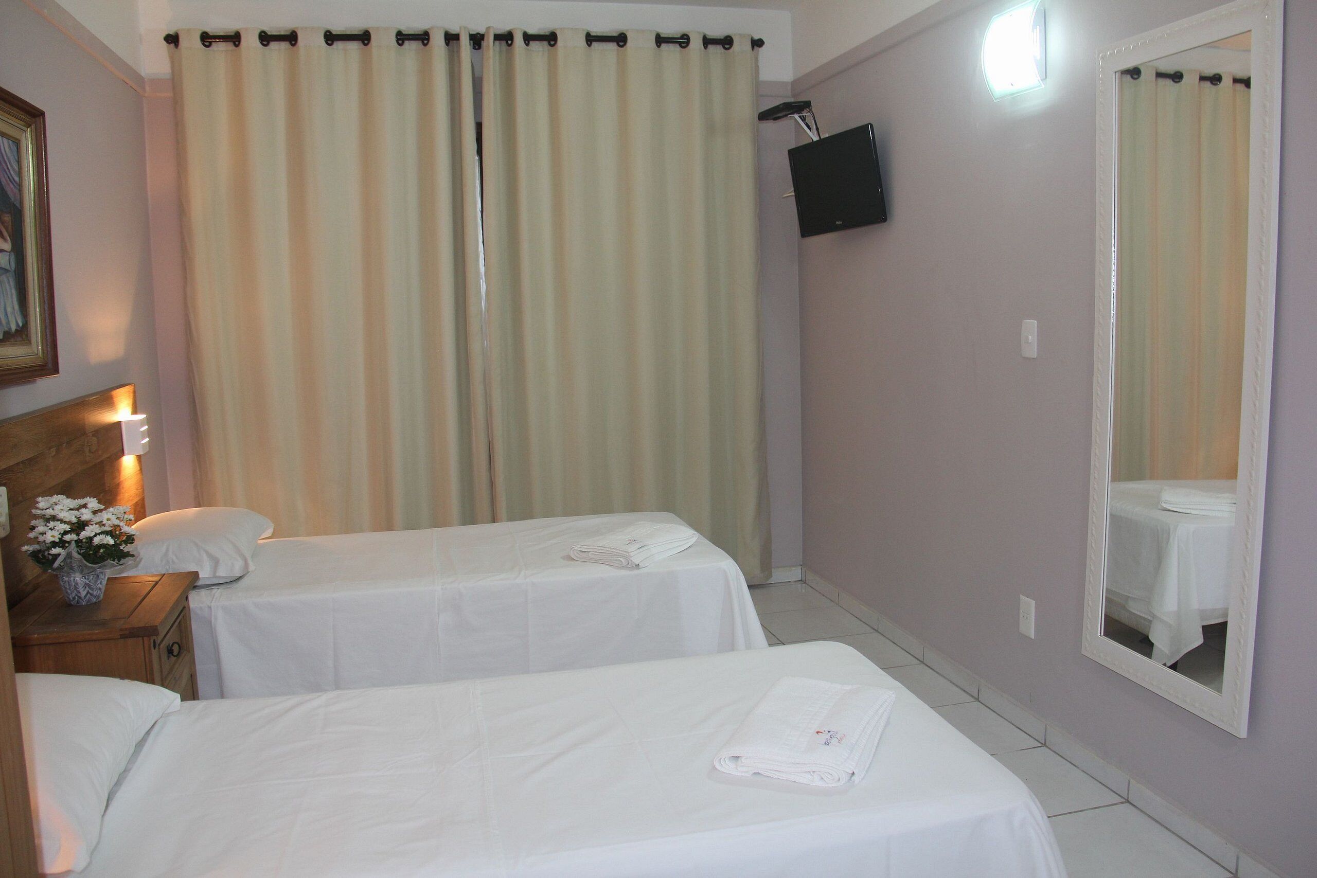 A hotel room with two beds, a TV mounted on the wall, and a mirror reflecting the room.