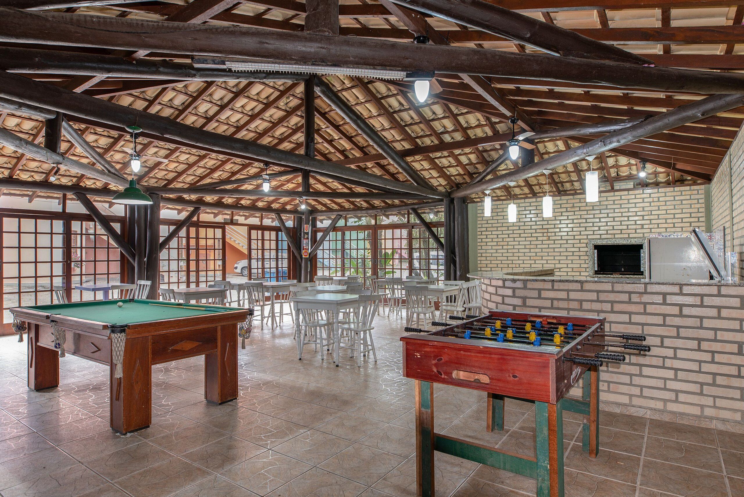 Un grand espace intérieur comprenant une table de billard, un baby-foot, ainsi que plusieurs tables et chaises blanches.