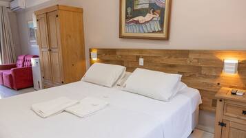 Habitació d'hotel amb un capçal de llit de fusta, un quadre damunt del llit, una cadira vermella i un armari de fusta.