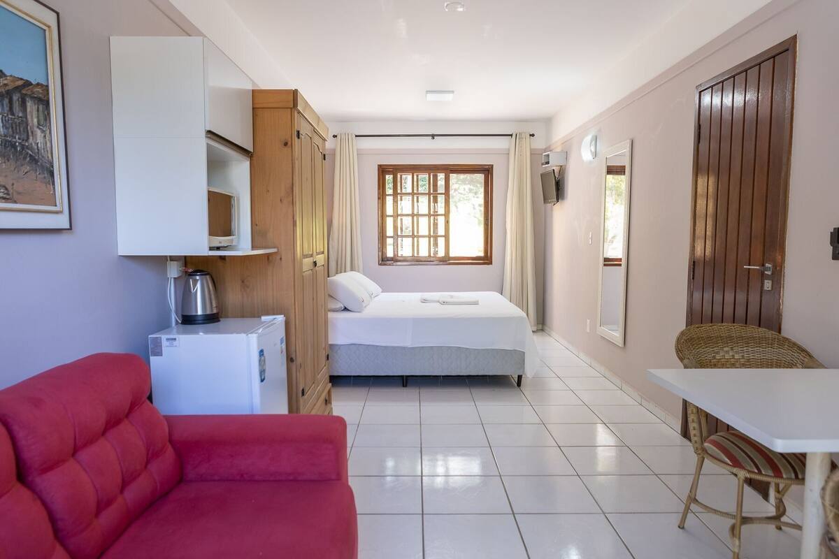 Una habitación compacta con una cama, un sofá rojo, una mesita y una kitchenette.