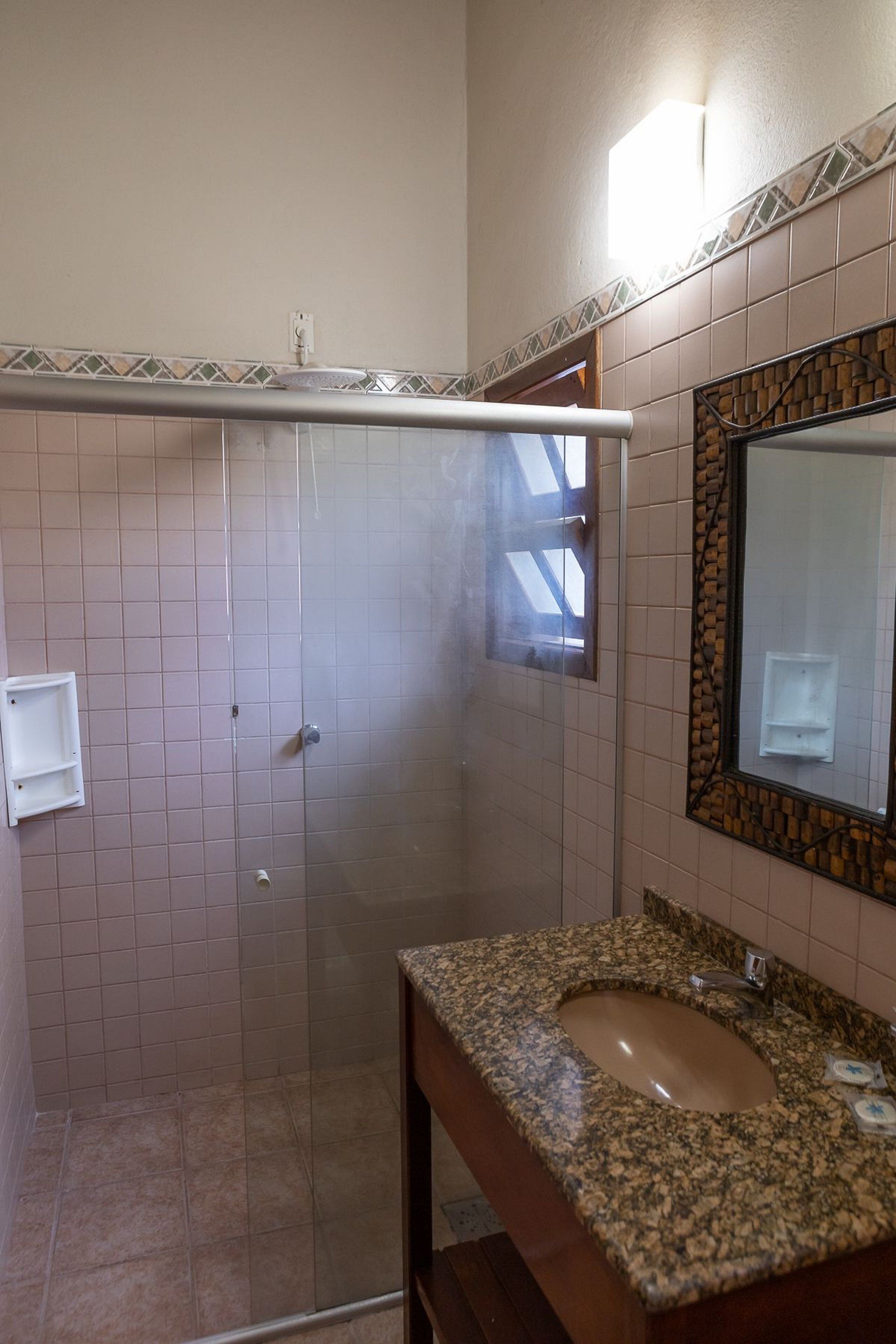 A bathroom with a glass-enclosed shower, a sink with a granite countertop, and a mirror with a decorative frame.