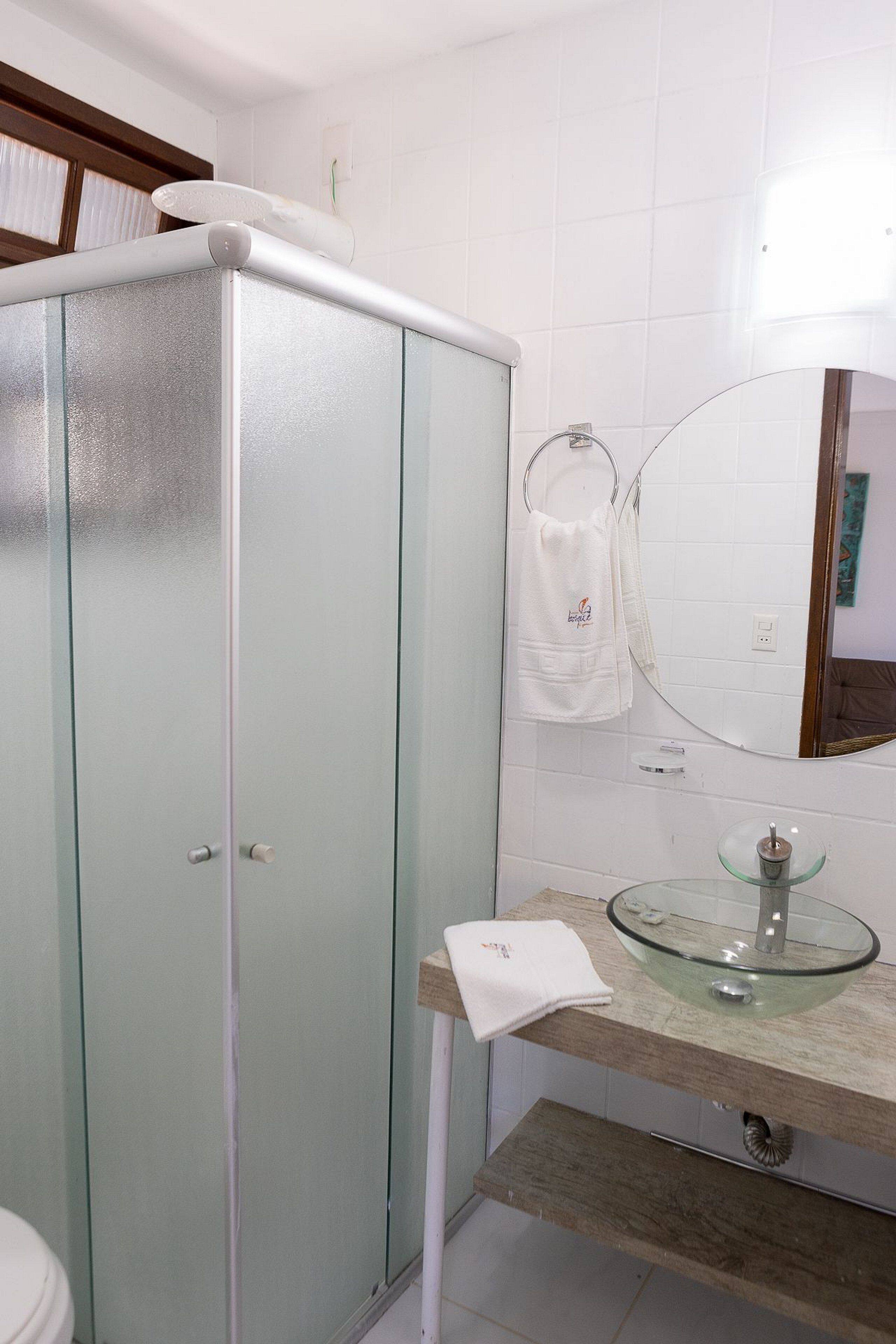 A bathroom with a glass-fronted cabinet, a round glass sink, and a mirror above the sink.