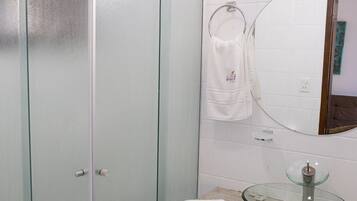 A bathroom with a glass-fronted cabinet, a round glass sink, and a mirror above the sink.