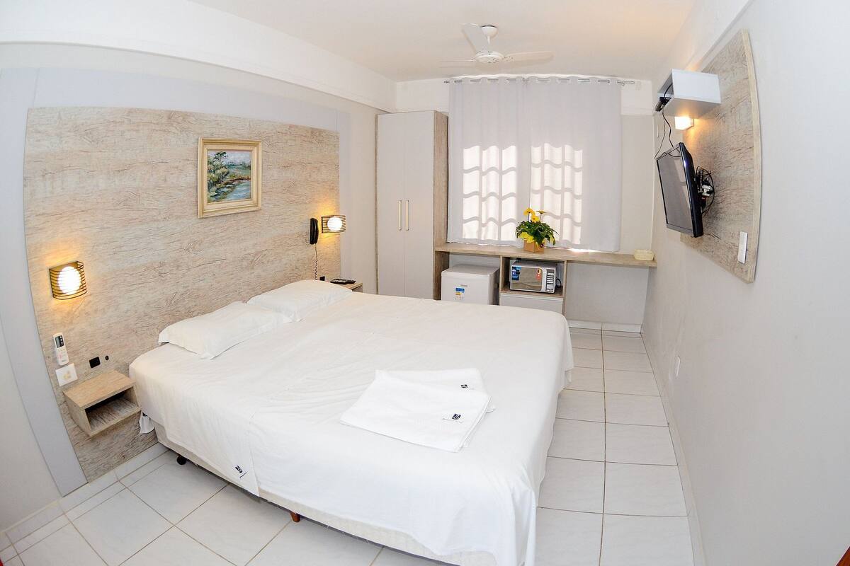 Habitación de hotel con una cama grande, una mesita de noche, teléfono en la pared, microondas y ventilador de techo.