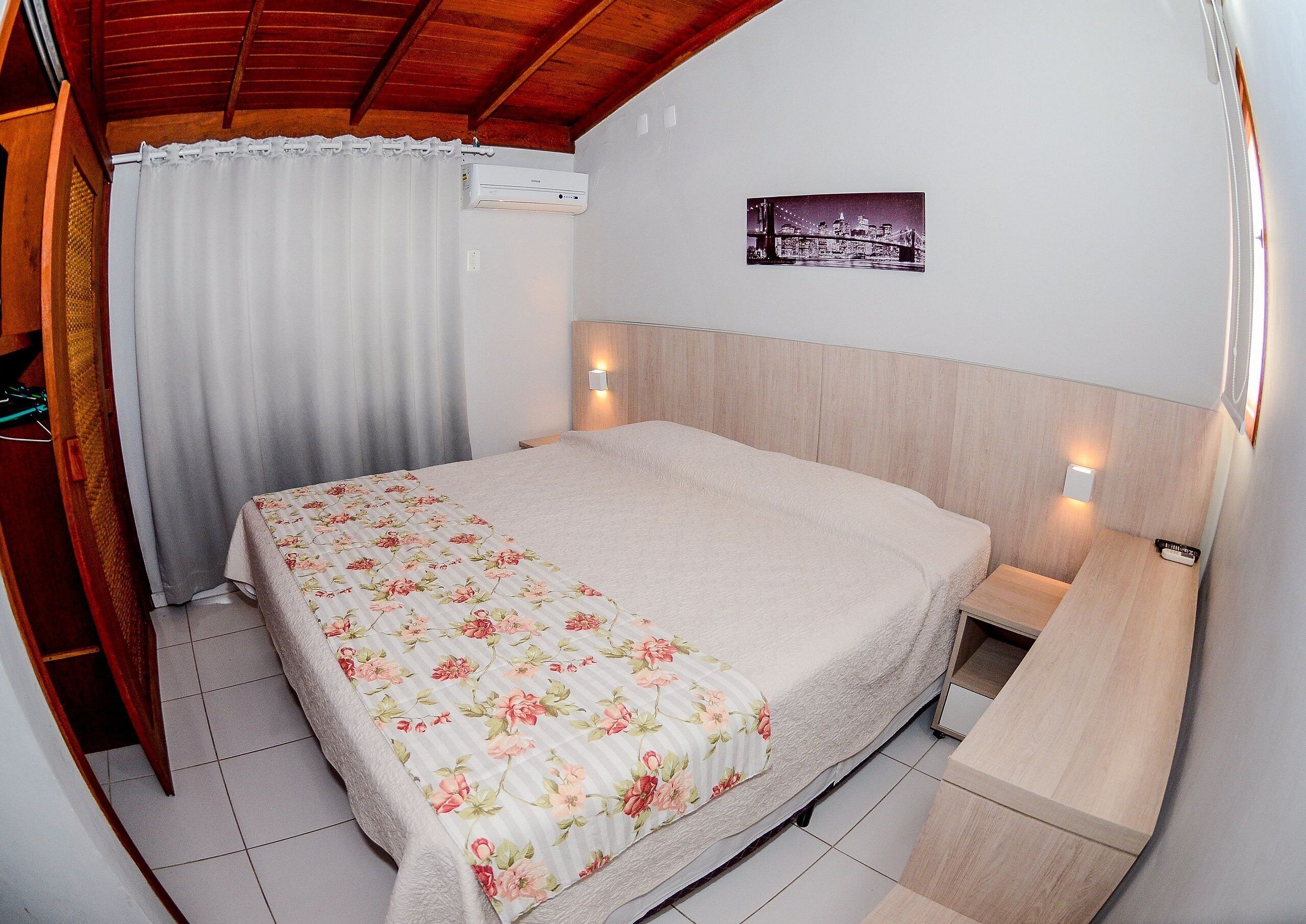 A bedroom with a bed, a nightstand, a wall-mounted air conditioner, and a picture on the wall.