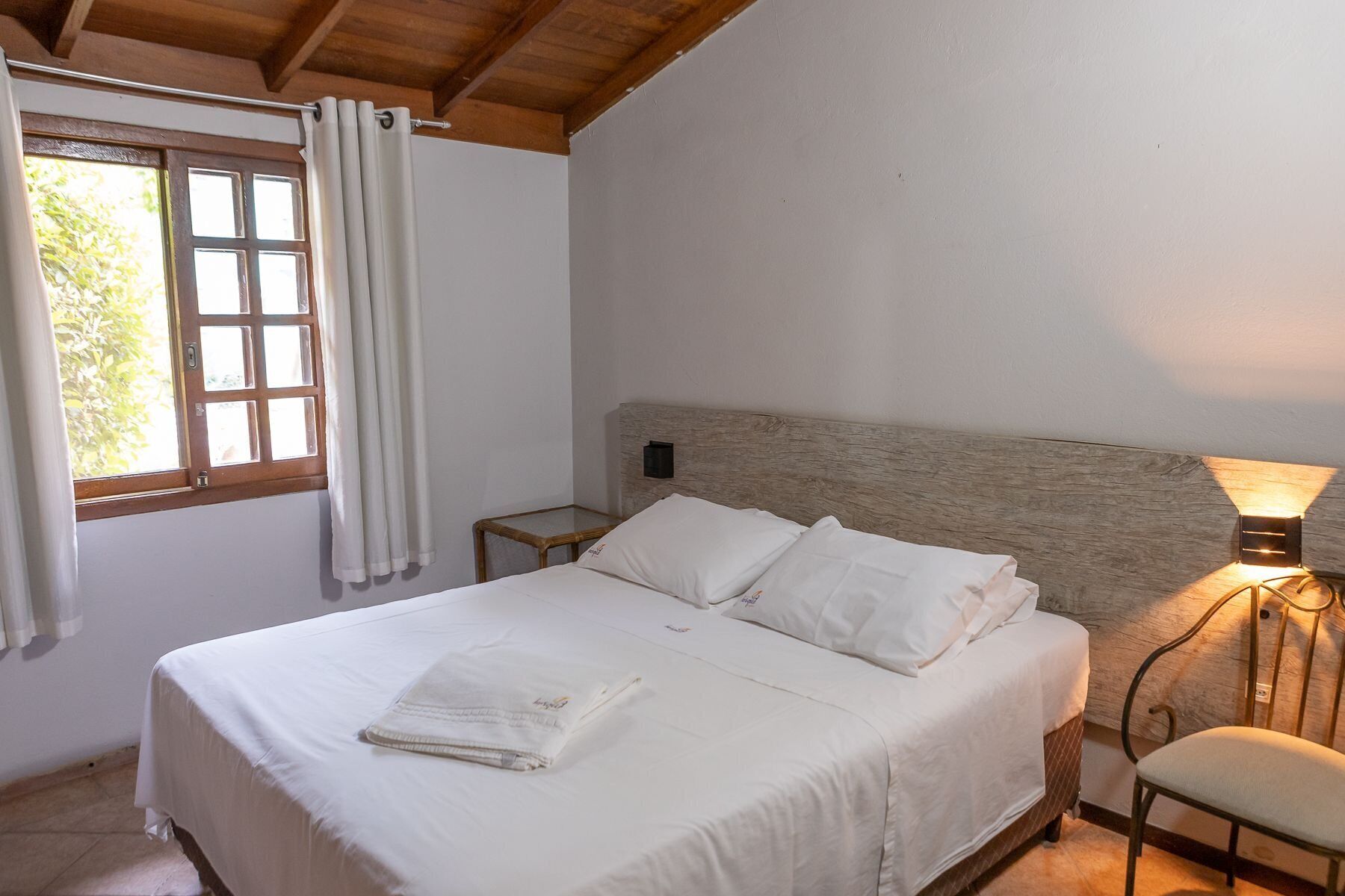 A bedroom with a bed, a nightstand, a lamp, and a window with curtains.