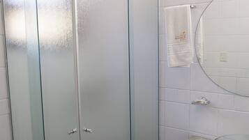 A bathroom with a glass-enclosed wardrobe, a round mirror, and a wooden vanity with a glass top.