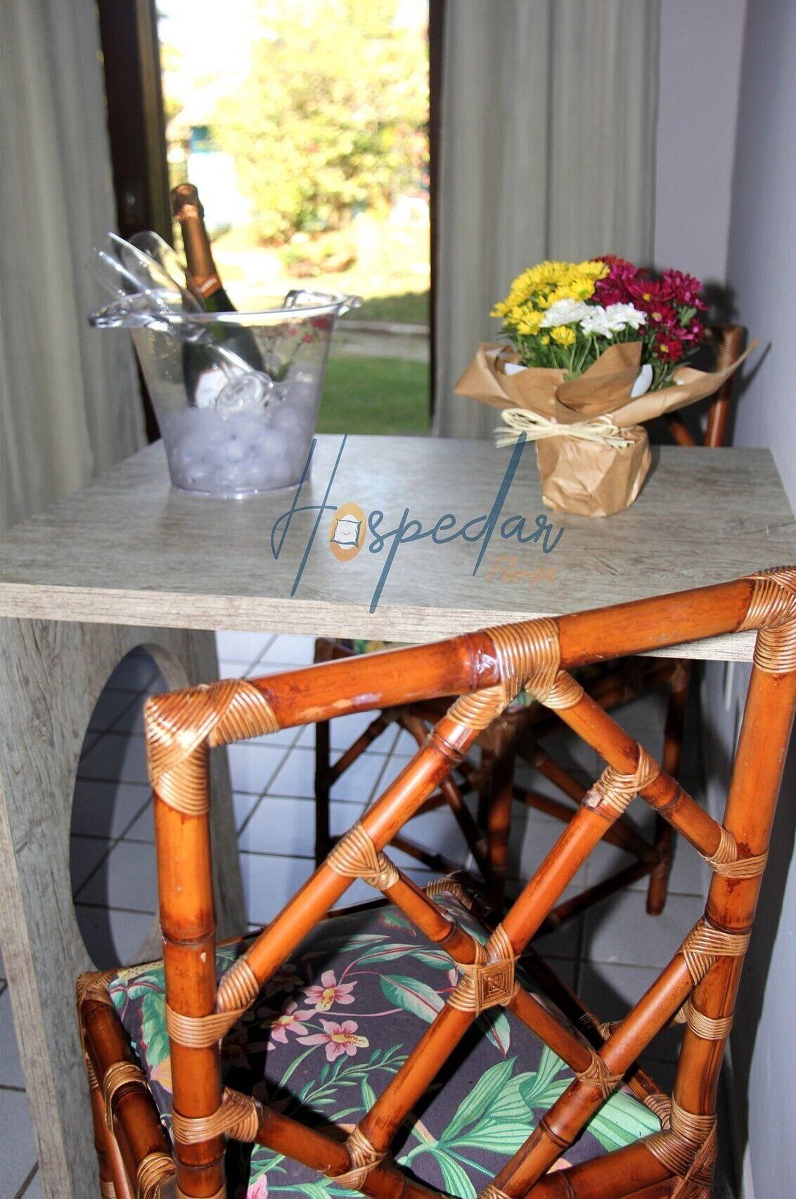 A table with a glass of champagne, a bouquet of flowers, and a wicker chair.