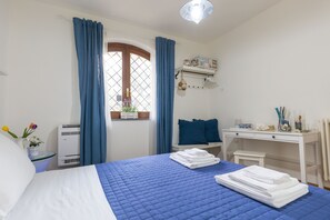 Habitación de hotel con cama, escritorio, silla, mesita, ventana con cortinas e iluminación en el techo.